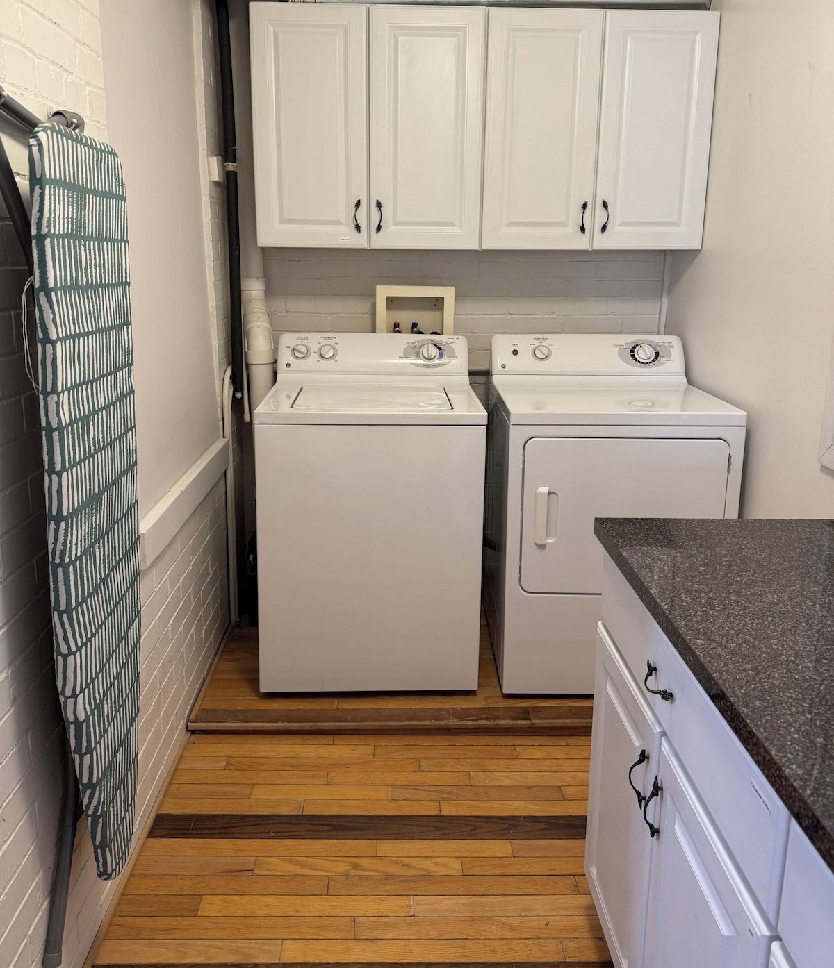 A laundry room with two white washing machines, a dryer, and a countertop with a sink.