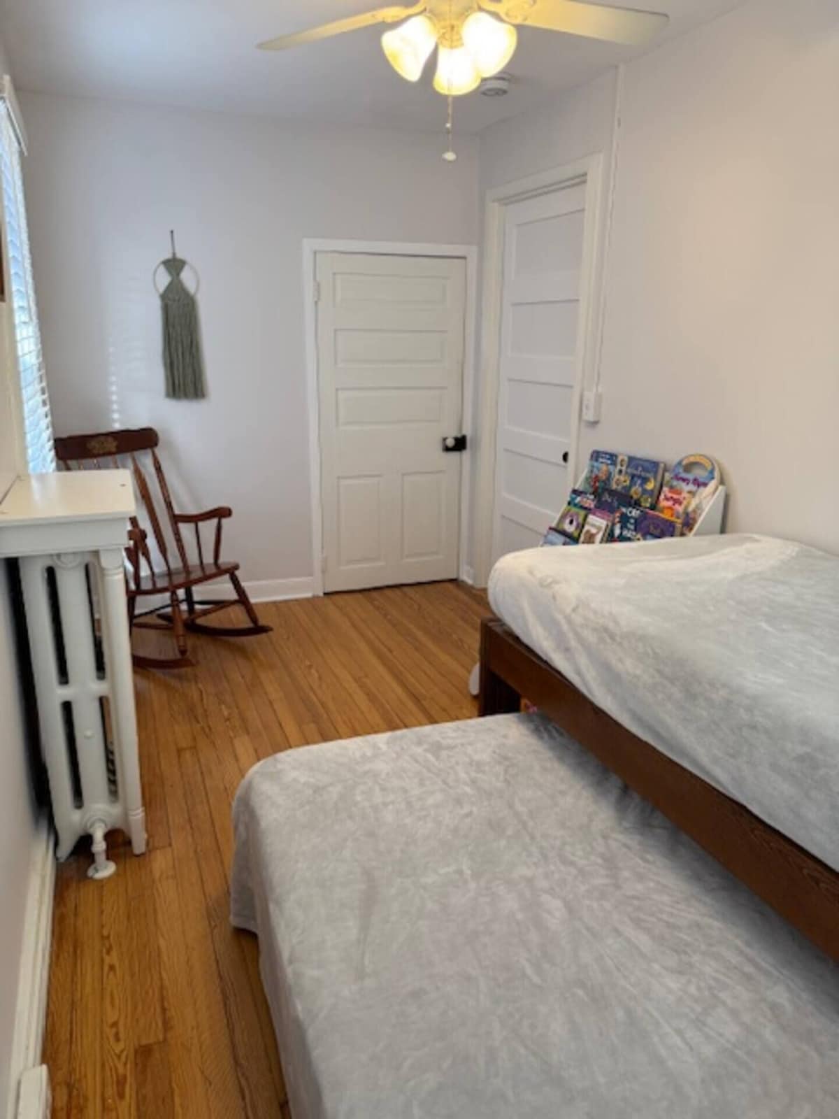 A bedroom with two beds, a rocking chair, a radiator, and a door.