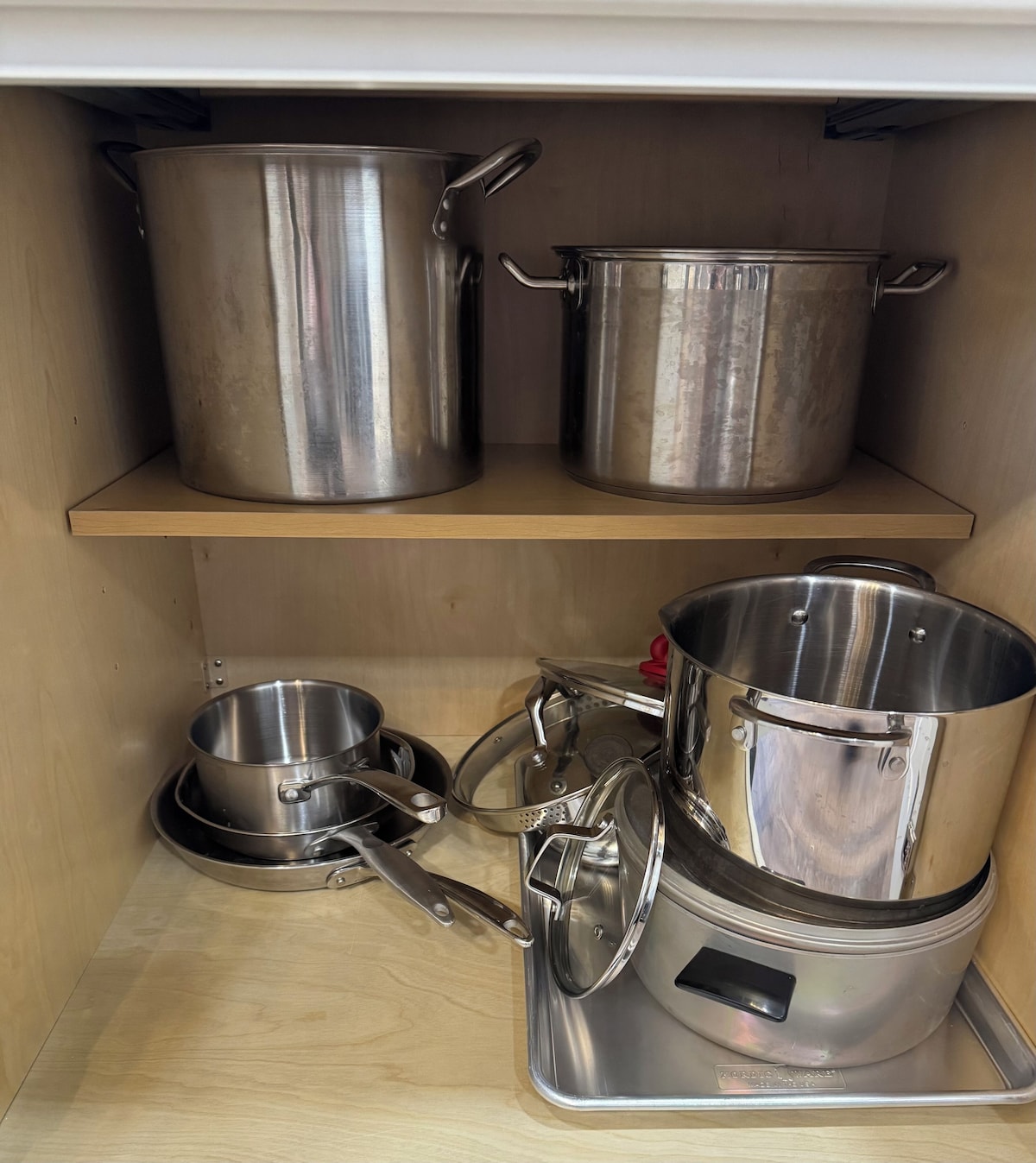 A kitchen shelf with stainless steel cookware including pots, pans, and a slow cooker.