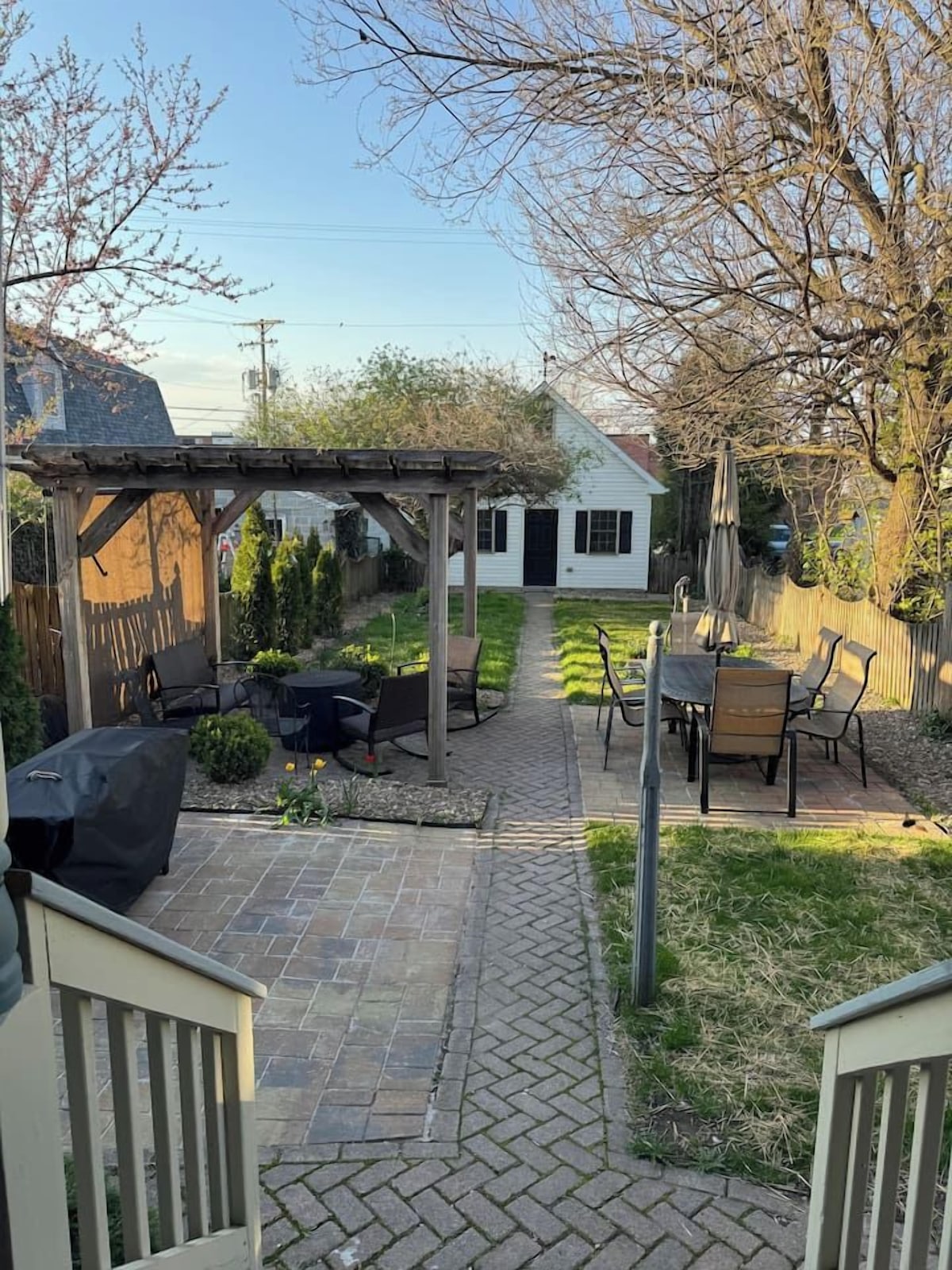 A backyard patio area with a pergola, outdoor seating, and a pathway leading to a house.