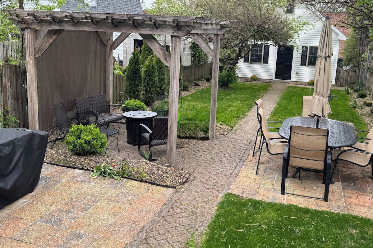 A patio with a pergola, two tables with chairs, and a covered grill area.