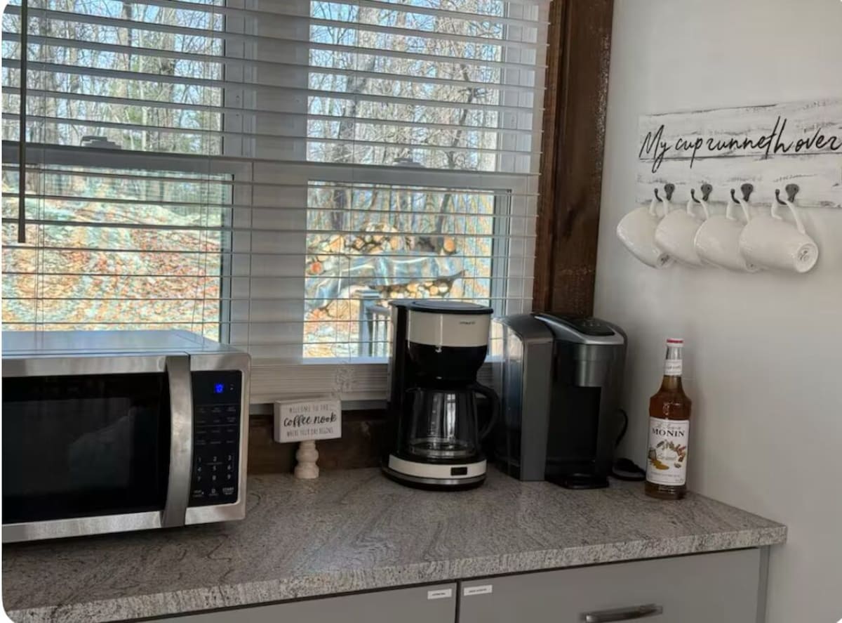A kitchen with a microwave, coffee maker, and a bottle of Monin syrup on the counter.