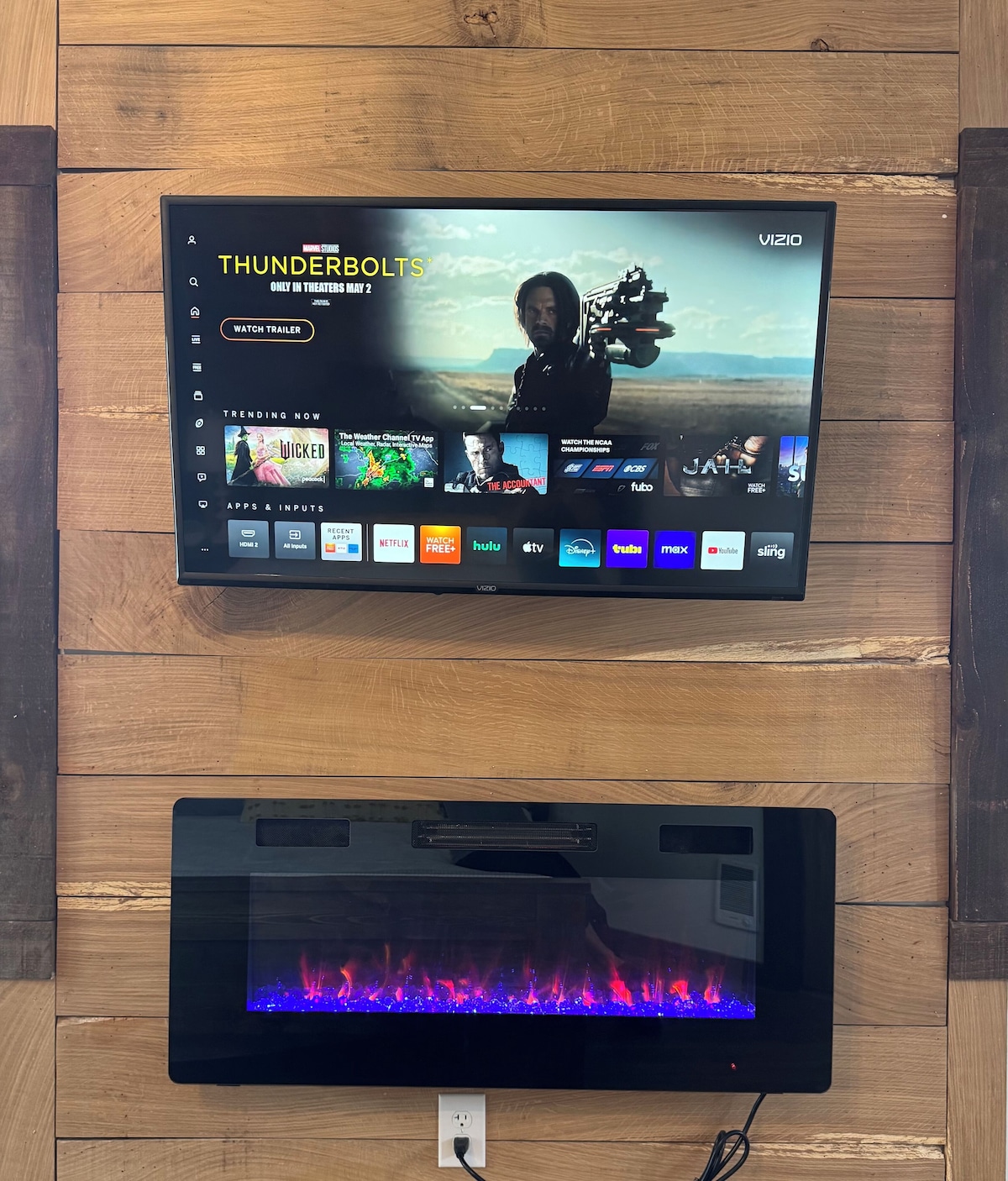 A flat-screen TV mounted on a wooden wall displaying a streaming interface with various apps and a movie title.