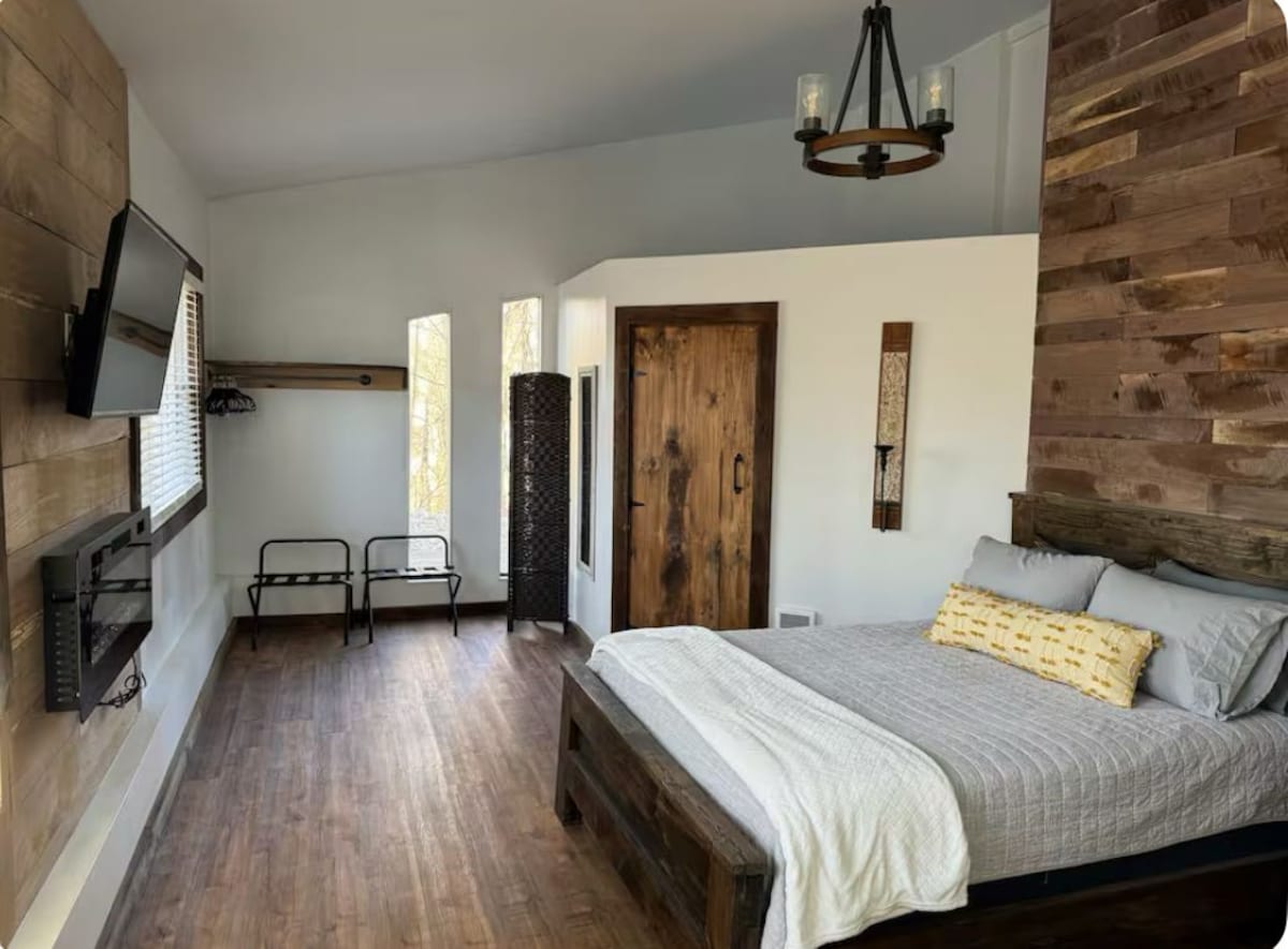 A bedroom with a large bed, a wooden headboard, a TV mounted on the wall, and a wooden floor.