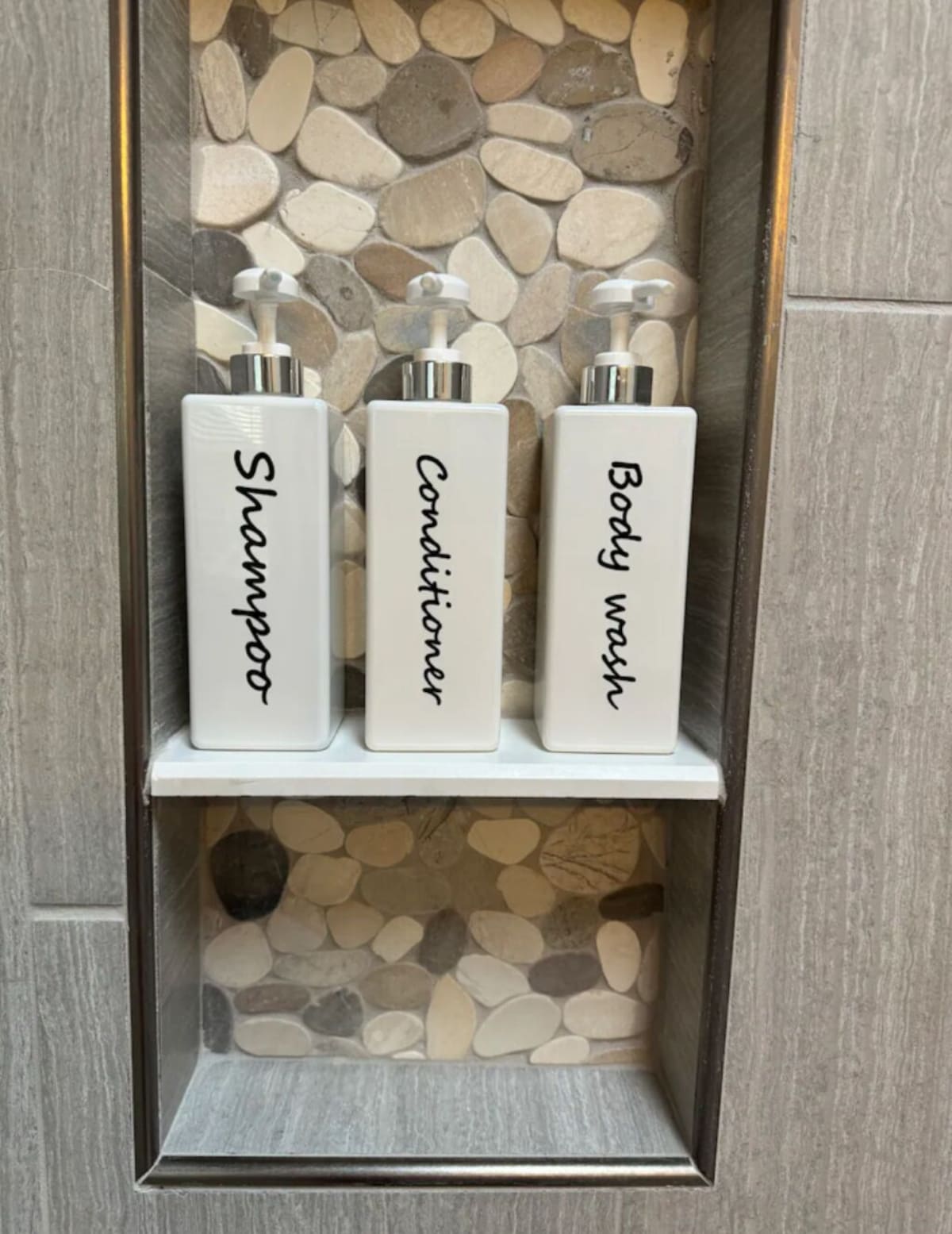 A bathroom shelf with three toiletry bottles labeled 'Shampoo,' 'Conditioner,' and 'Body wash.'