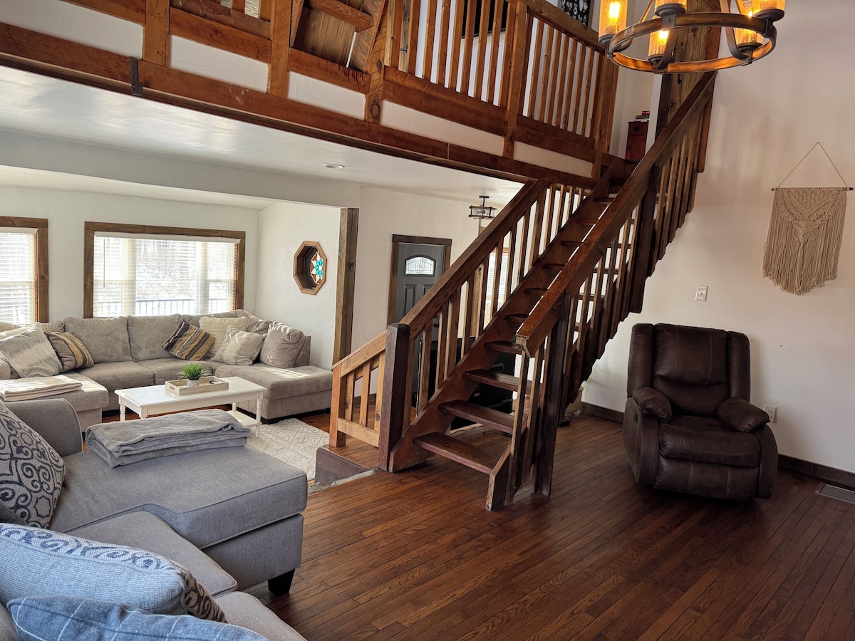 A spacious living room with a wooden staircase, a sofa set, and a leather armchair.
