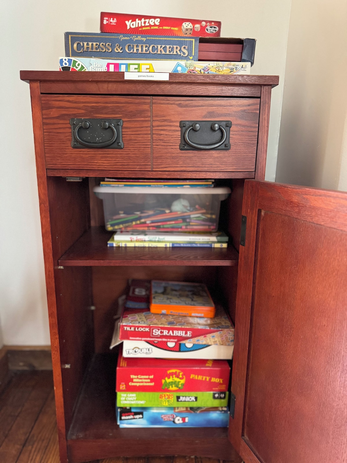 A wooden cabinet with two drawers and a shelf, containing various board games and books.