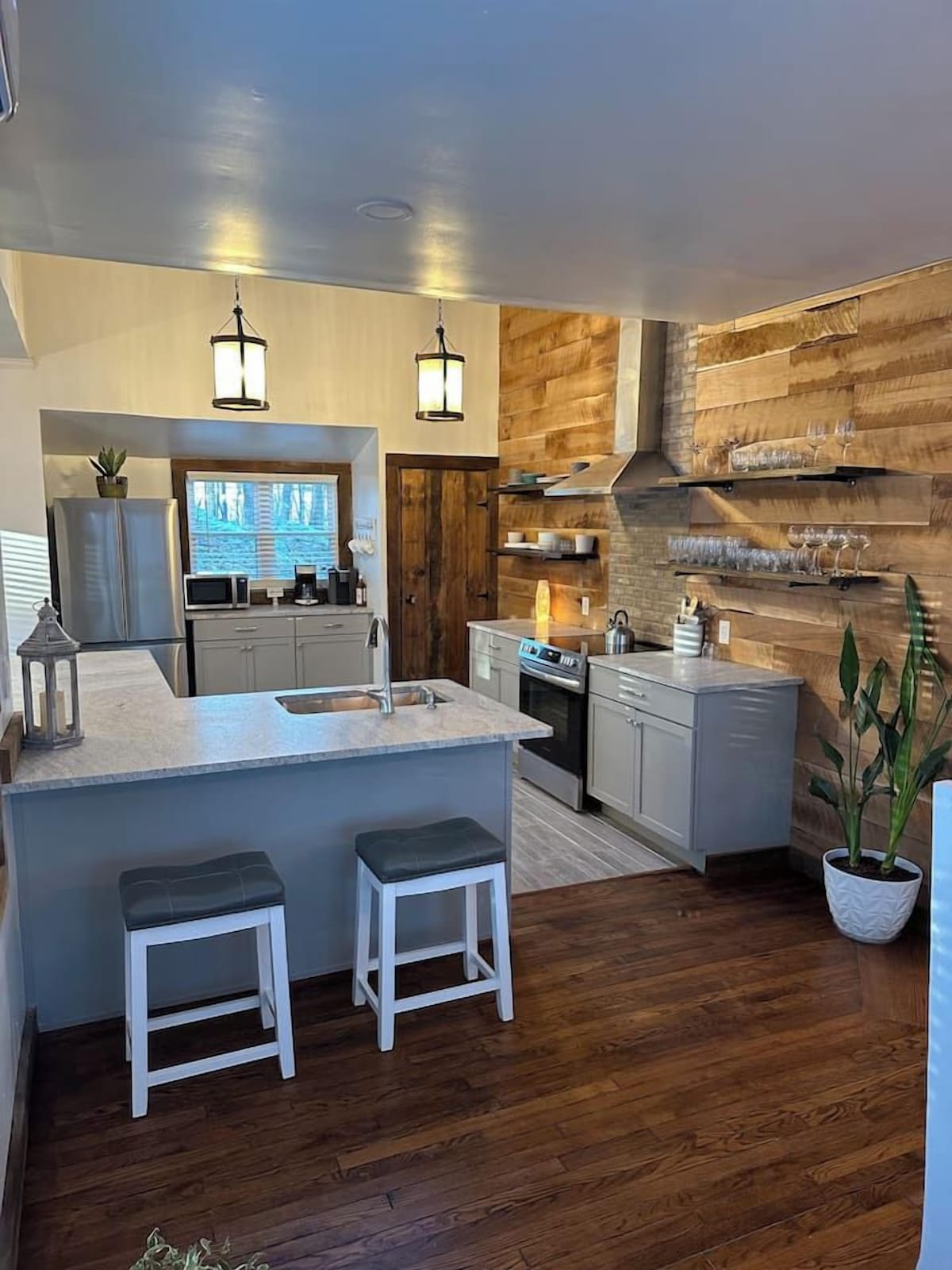 A modern kitchen with a central island, bar stools, wooden wall paneling, and built-in appliances.