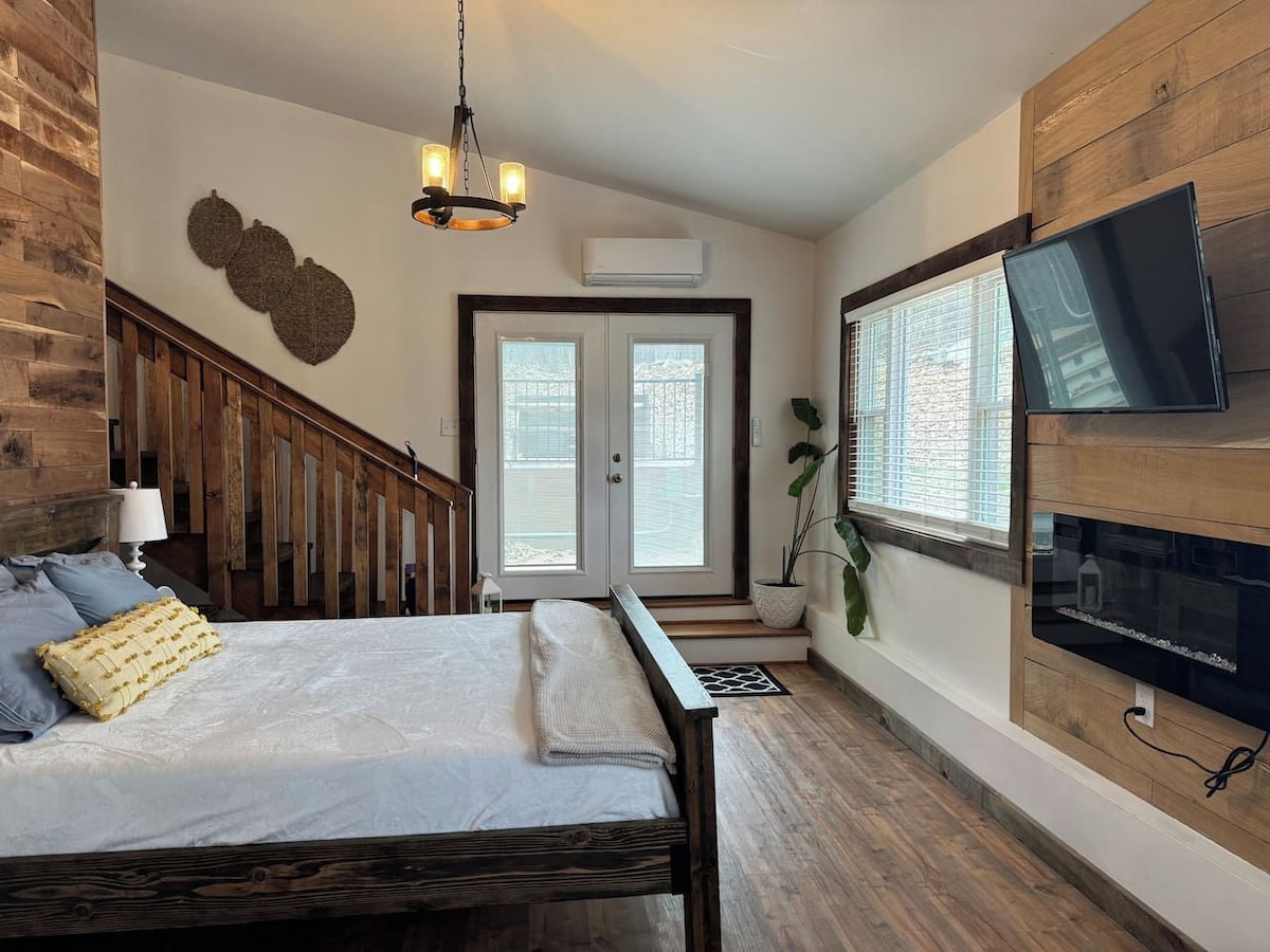 A bedroom with a bed, a TV mounted on the wall, a staircase, and a door leading to a balcony.