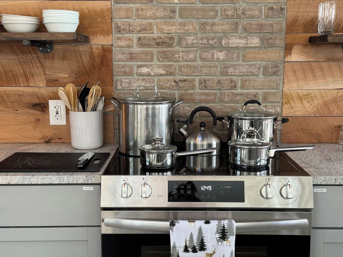 A kitchen with a brick wall, stainless steel appliances, and a white towel with a forest print hanging from the oven handle.