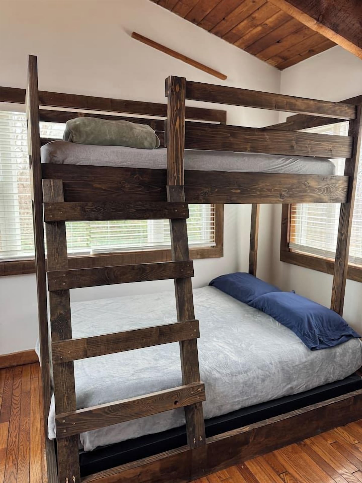 A bunk bed with a wooden ladder, a grey mattress, and a blue pillow.