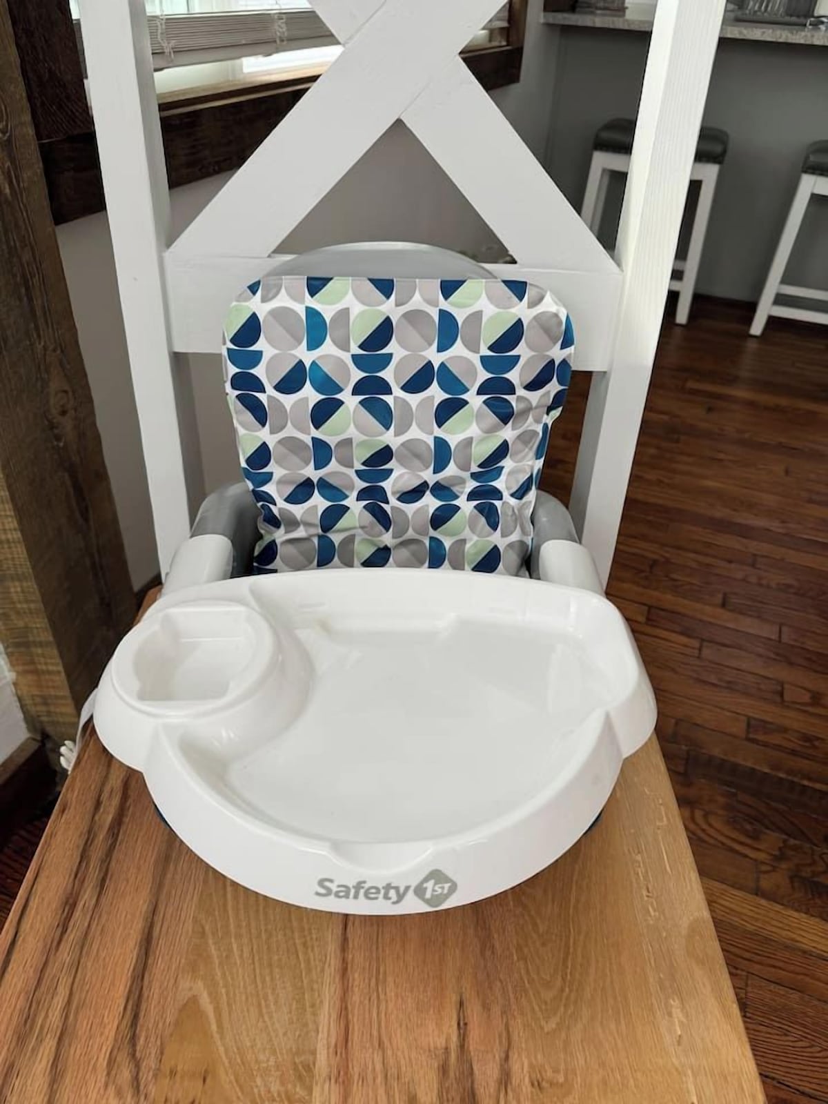 A baby high chair with a patterned seat and a tray table, placed on a wooden table.
