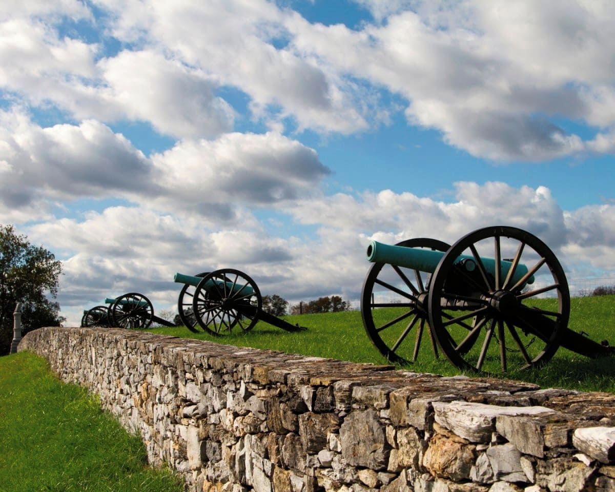 A stone wall with cannons on a grassy field under a partly cloudy sky.